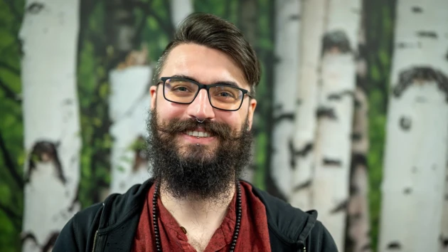 A man with a beard and glasses in front of a birch tree wallpaper background