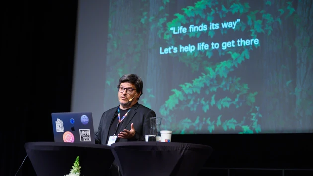 Ricard Solé, public speaker for the 15 year IceLab anniversary public lecture on terraforming ecosystems, seen here against an AI-generated backdrop depicting an arid ecosystem being transformed to a lush one thanks to synthetic organisms.