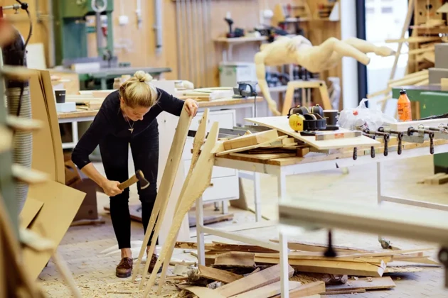 En student på Konsthögskolan är i en ateljé och jobbar med sitt konstverk i trä.